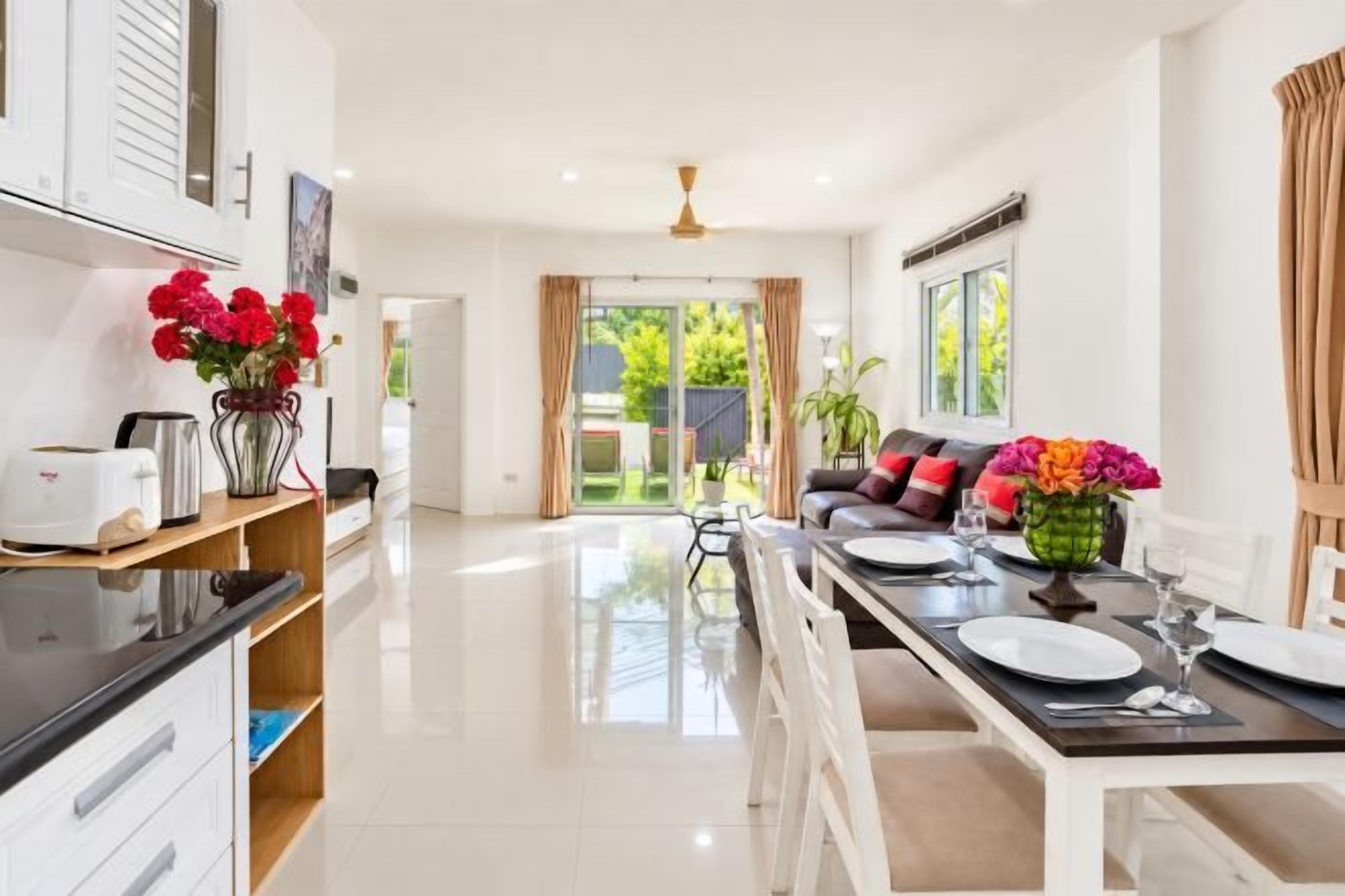 A modern kitchen with a dining area, a sofa set, and a view of the outdoors.