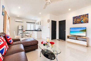 A modern living room with a sofa, a glass coffee table, and a flat-screen TV on a wooden stand. - Chalong Hideaway Pool Villa (Phuket)