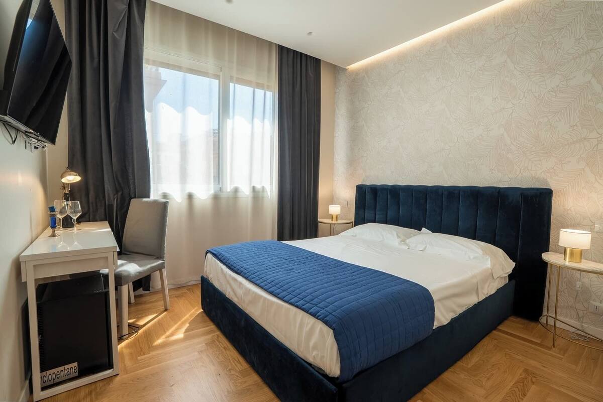 A hotel room with a bed, a desk, a chair, a TV, and a window with curtains.