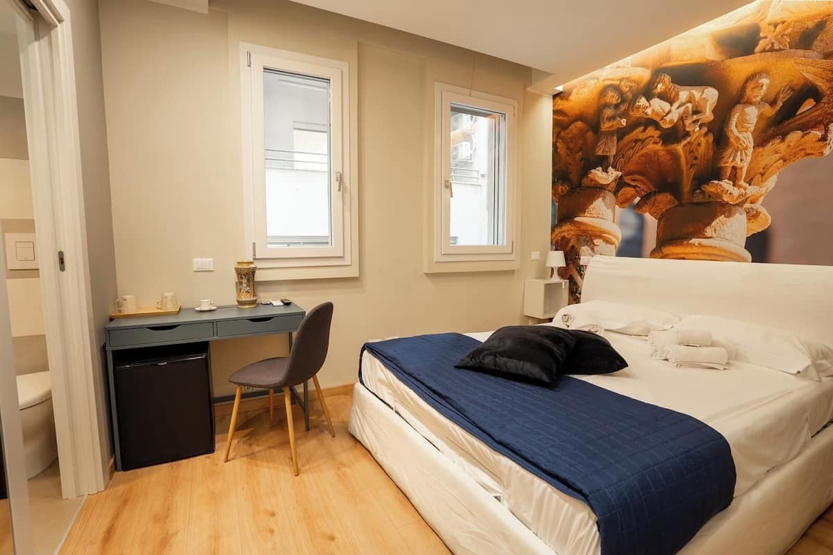 A bedroom with a bed, a desk, a chair, and a small kitchenette.