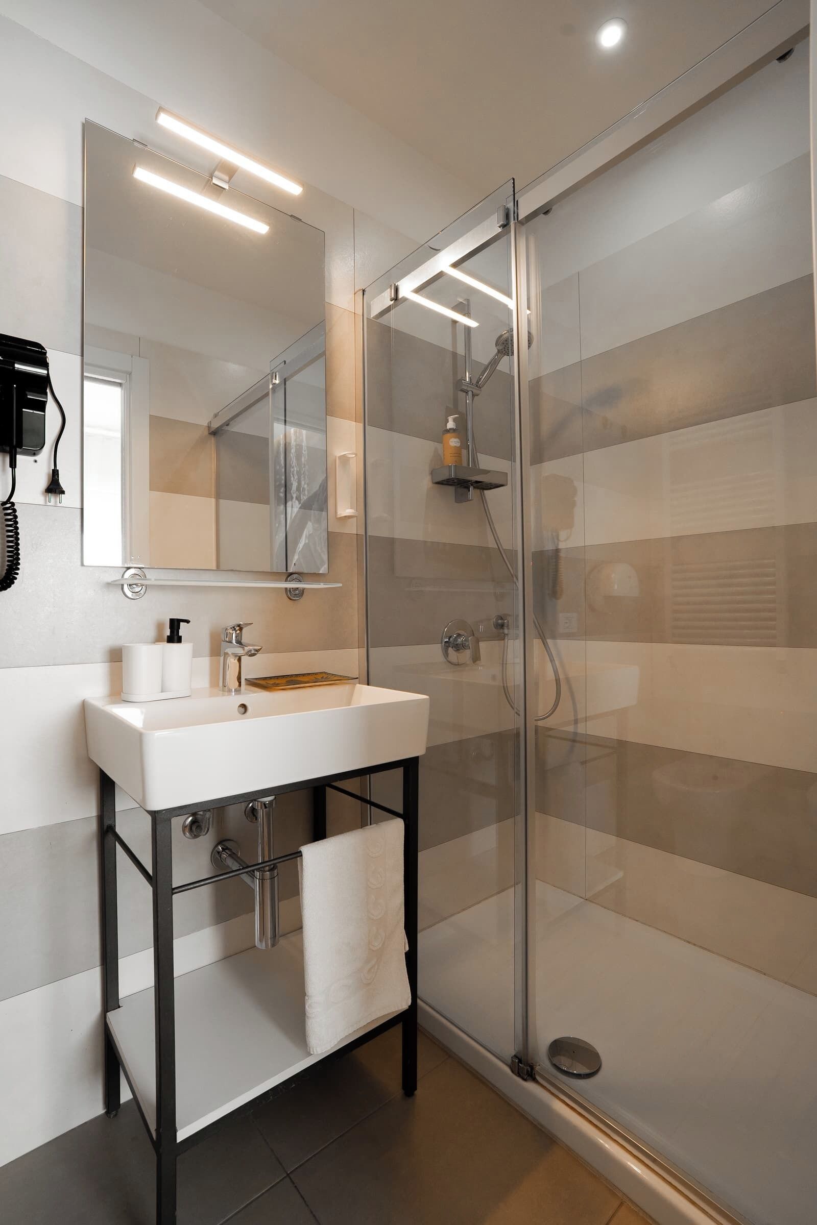 A modern bathroom with a glass-enclosed shower, a white sink, and a mirror above it.
