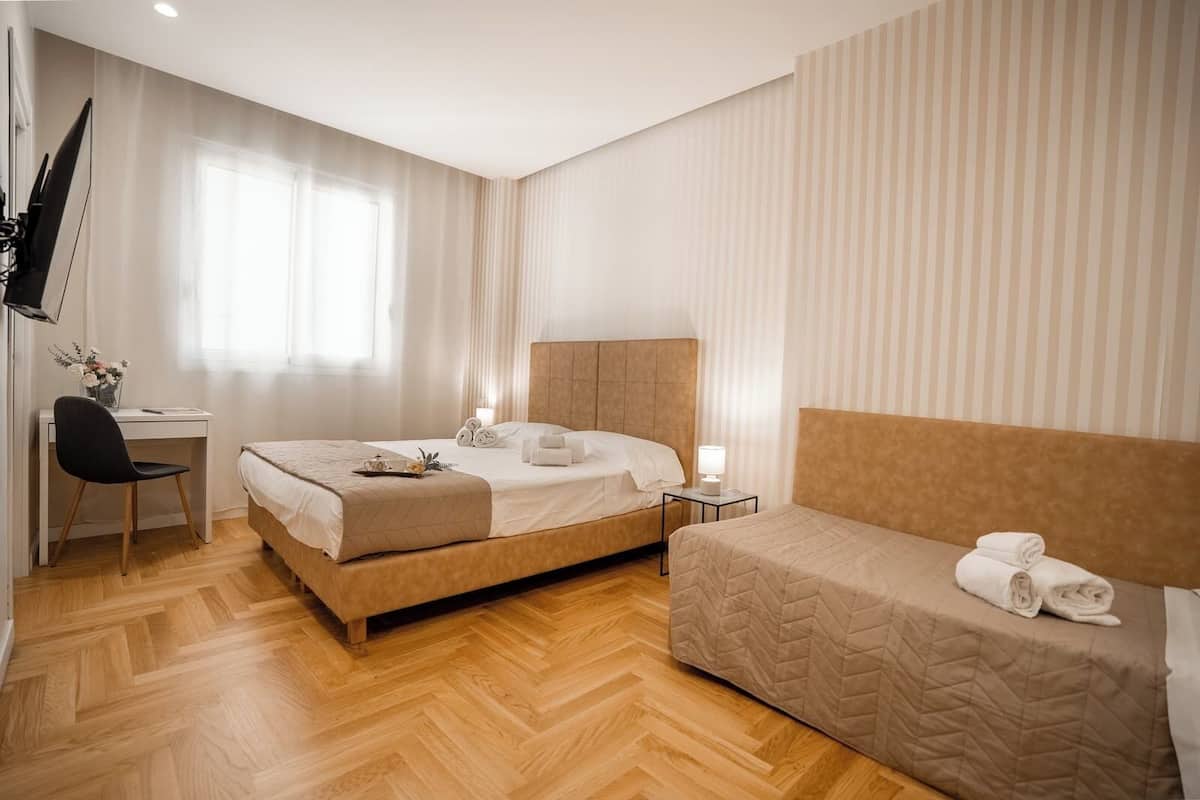A hotel room with a large bed, a smaller bed, a desk with a chair, a TV, and a window with curtains.