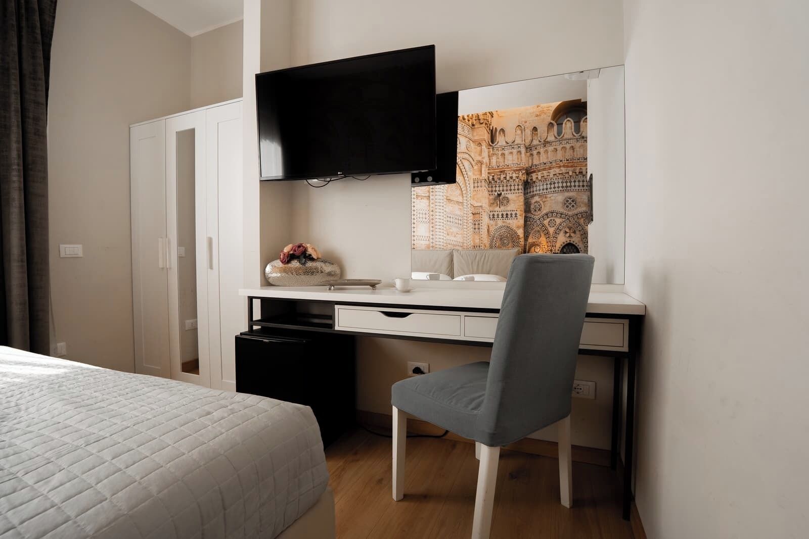 Un dormitorio con una cama, un escritorio con una silla, un televisor y un espejo decorativo.