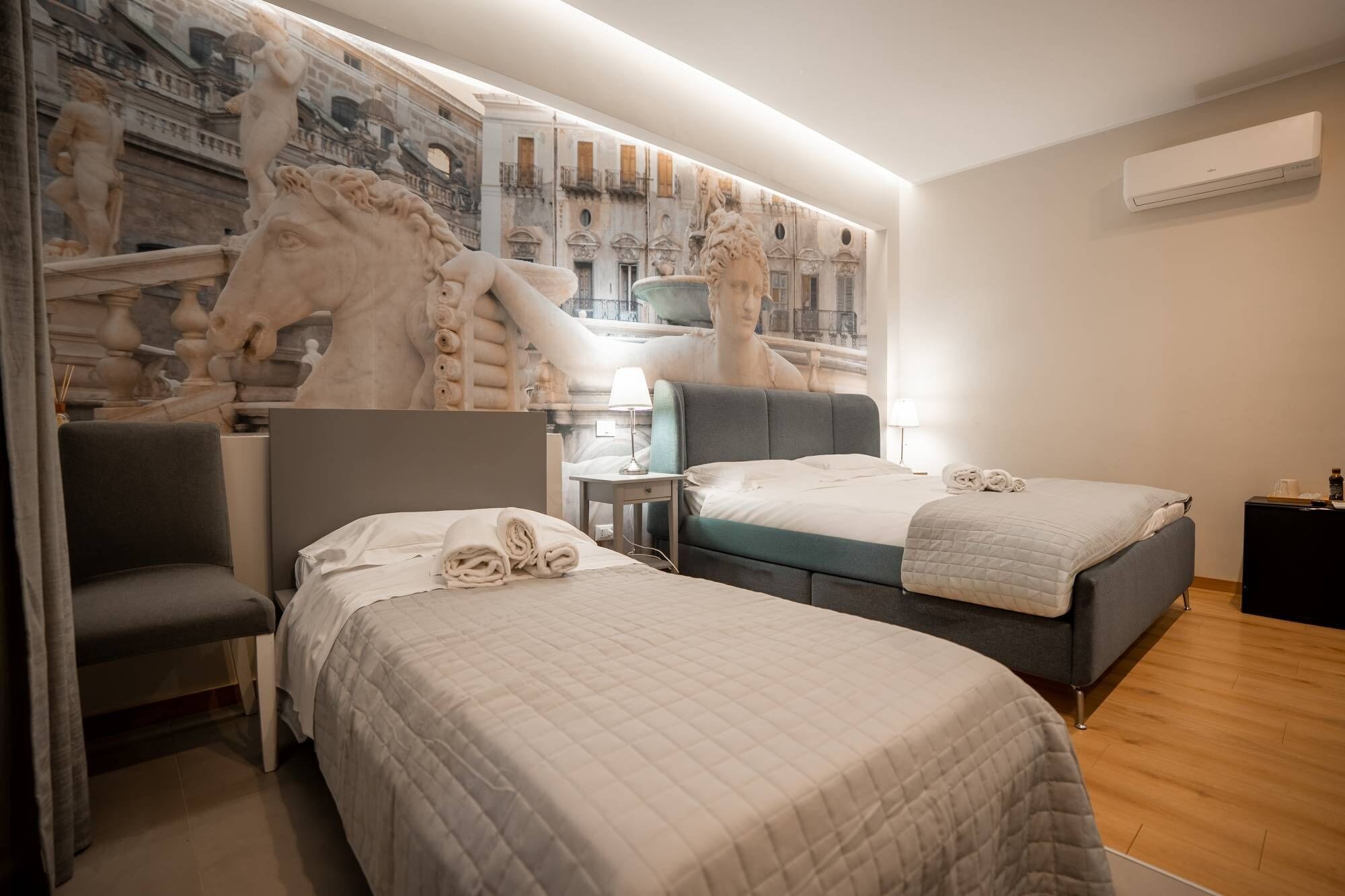 A hotel room with two beds, a chair, a nightstand, and a large mural on the wall.