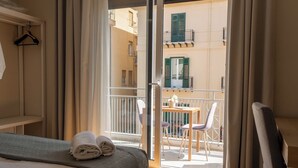 Habitació d'hotel amb llit, taula i cadires, i un balcó amb vista a edificis.