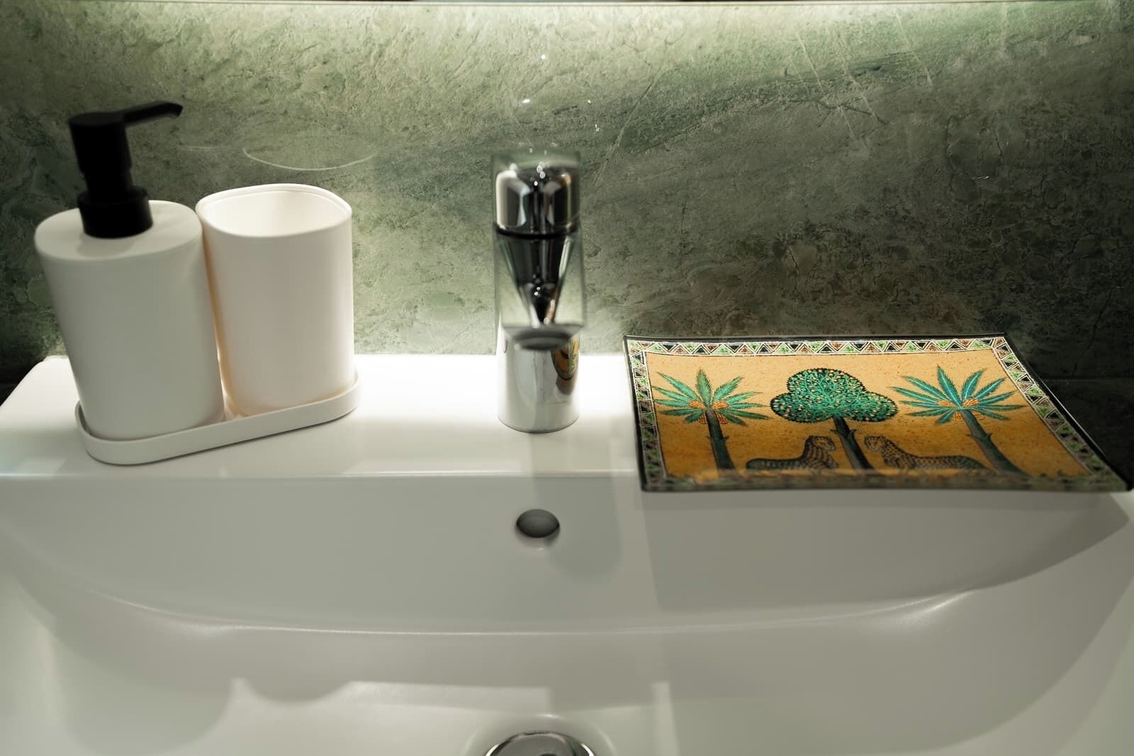 A bathroom sink with a soap dispenser, a faucet, and a decorative tile.