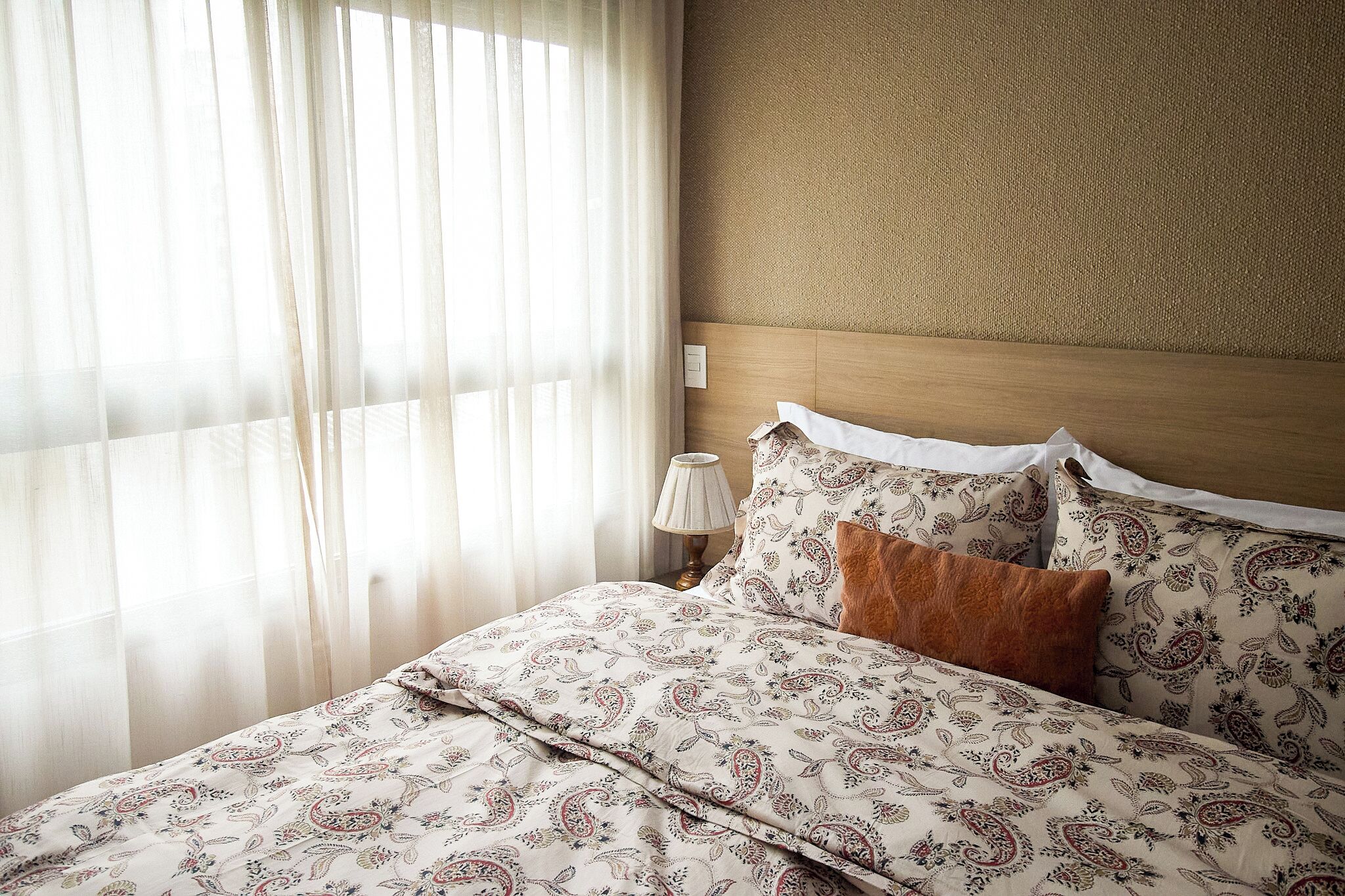 A neatly made bed with a patterned bedspread, a wooden headboard, and a bedside lamp.