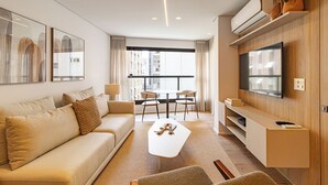 Ein modernes Wohnzimmer mit Sofa, Couchtisch und Fernseher. Es gibt einen Essbereich mit Stühlen und einem Tisch.
