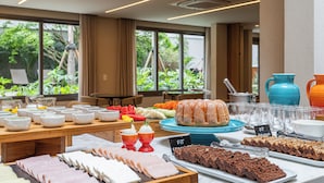 Ein reichhaltiges Buffet mit verschiedenen Speisen, darunter Fleisch, Brot und Desserts, präsentiert auf Tischen mit Blick auf eine grüne Landschaft.