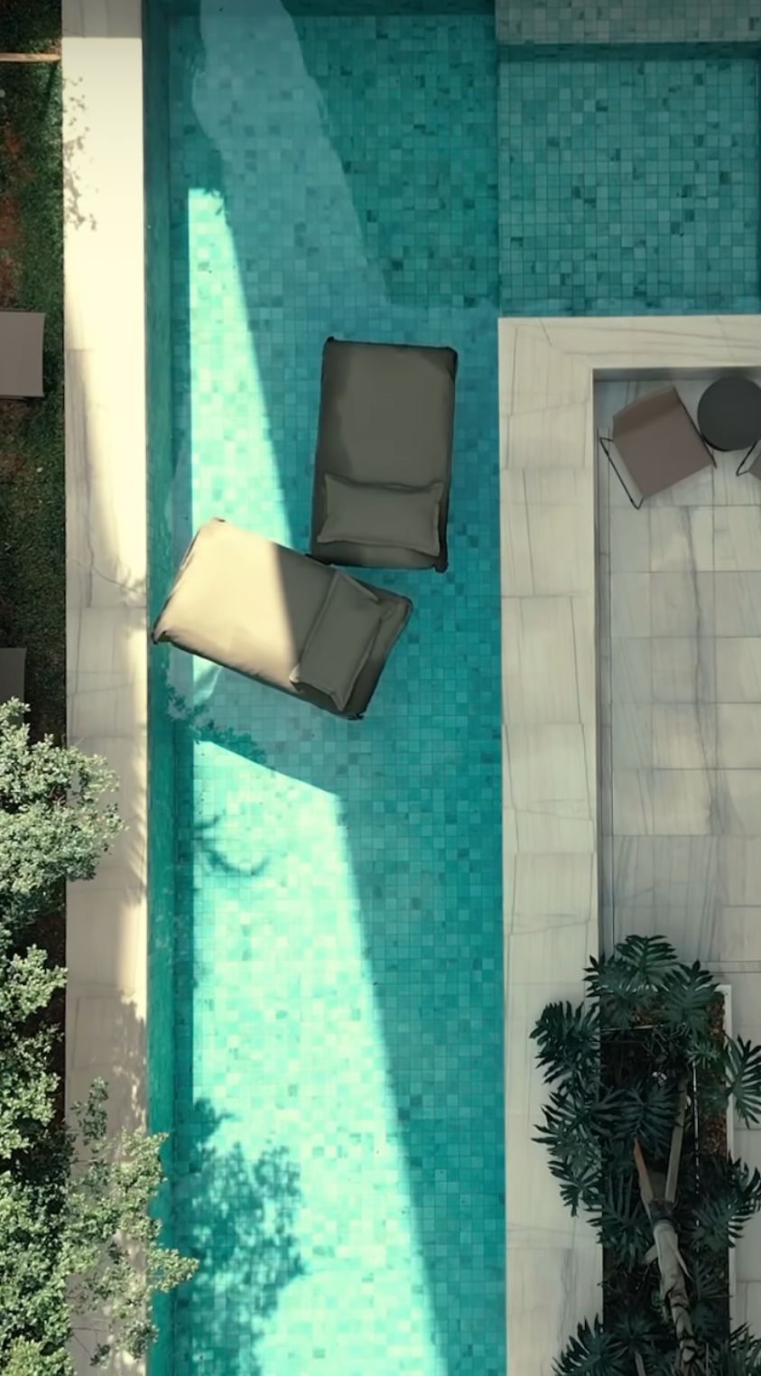 A rooftop pool with two lounge chairs and a small table, surrounded by greenery and a tiled deck.