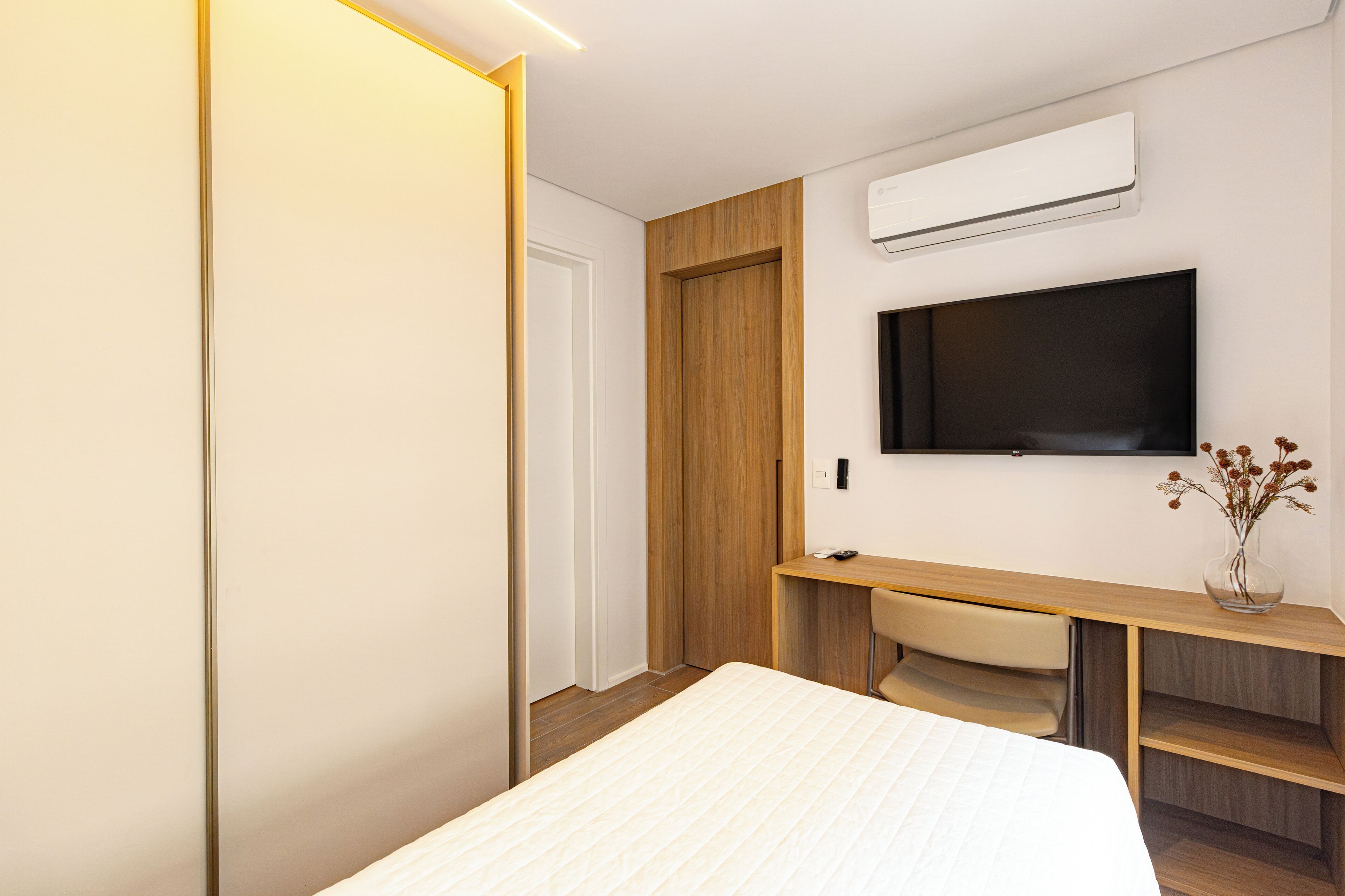 A modern hotel room with a bed, a desk, a chair, and a mounted TV.