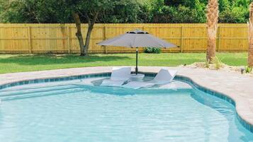 A swimming pool with a wooden deck, a palm tree, and a wooden fence in the background.