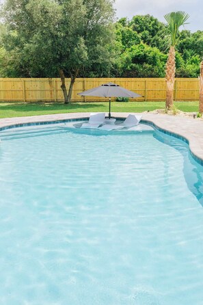 Une piscine avec une terrasse en bois, un palmier et une clôture en bois en arrière-plan.