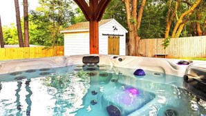 A hot tub with built-in jets, surrounded by a wooden deck and a white shed in a backyard. - Hot Tub Hideaway for pets and family (Pensacola)
