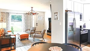 A modern living room with a dining area, a kitchen with stainless steel appliances, and a large window with patterned curtains. - Hot Tub Hideaway for pets and family (Pensacola)