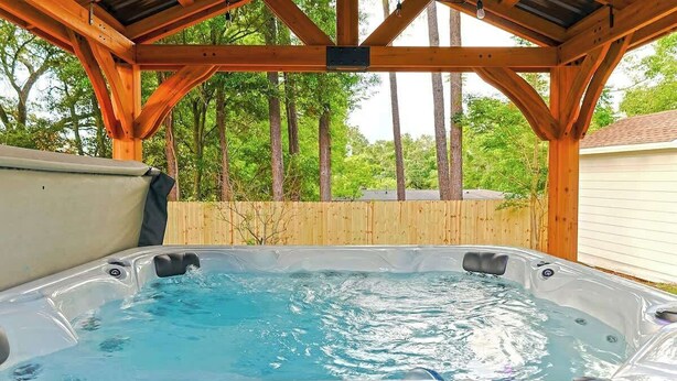 A hot tub under a wooden pergola with a wooden fence and trees in the background. - Hot Tub Hideaway for pets and family (Pensacola)