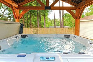 Un bain à remous sous une pergola en bois, avec une clôture en bois et des arbres en arrière-plan.