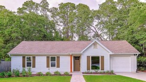 A single-story house with a front garage, a central door, and a small front yard with a pathway leading to the entrance. - Hot Tub Hideaway for pets and family (Pensacola)