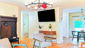 A living room with a fireplace, a television mounted on the wall, and a dining area with a table and chairs. - Hot Tub Hideaway for pets and family (Pensacola)
