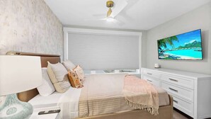 Een slaapkamer met een bed, nachtkastje, lamp, televisie en een raam met jaloezieën.