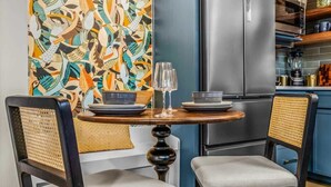 Een moderne keuken met een roestvrijstalen koelkast, een eettafel met stoelen en een kleurrijke abstracte wanddecoratie.