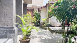 A courtyard with potted plants, a stone pathway, and a traditional building with a tiled roof. - Bejraee Kumar Guest House Ubud (Bali)