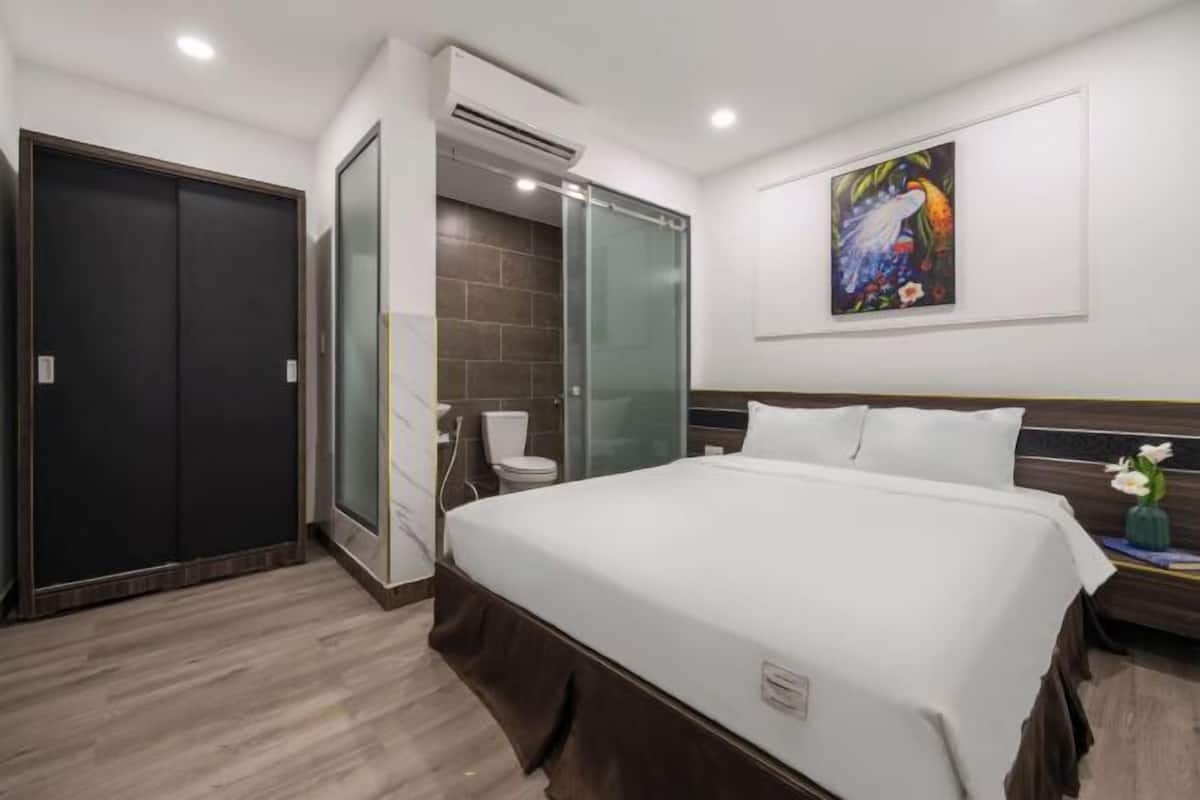 A hotel room with a bed, a shower, a toilet, and a painting on the wall.