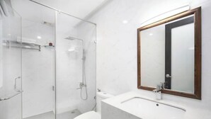 Une salle de bain moderne avec une douche à parois de verre, des toilettes blanches et un lavabo en marbre agrémenté d’un miroir encadré en bois.