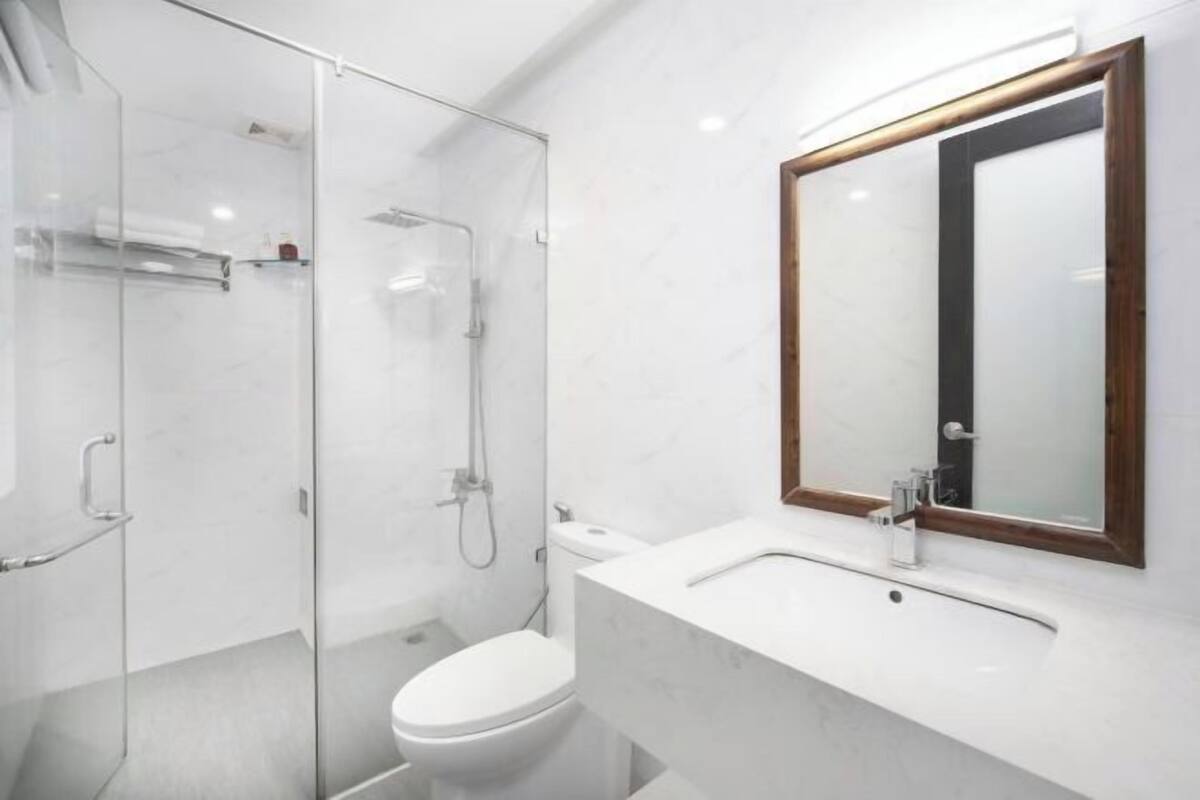 A modern bathroom with a glass-enclosed shower, a white toilet, and a marble sink with a wooden-framed mirror.