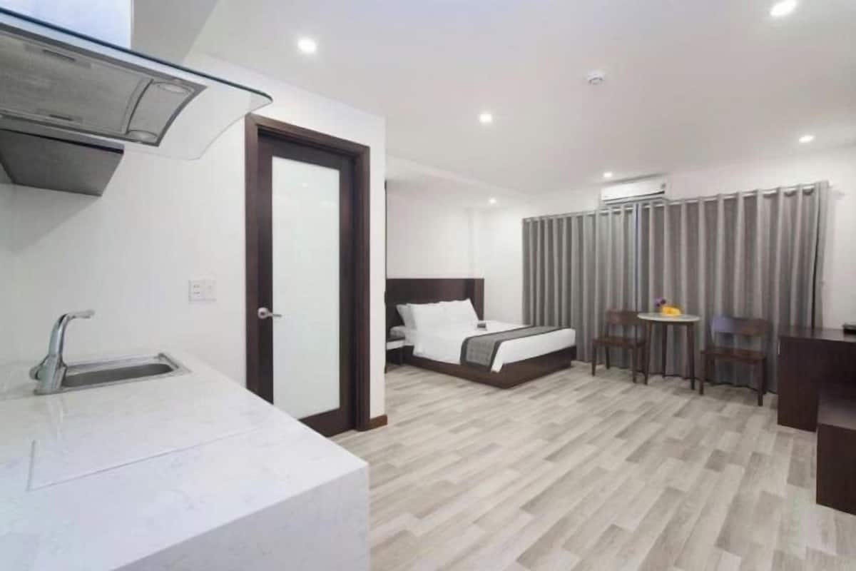 A hotel room with a bed, a small table, a chair, a desk, a sink, and a window with curtains.