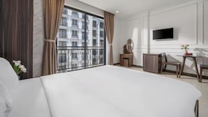 Une chambre d’hôtel avec un grand lit, un bureau avec une chaise, un téléviseur fixé au mur et un balcon offrant une vue sur la ville.