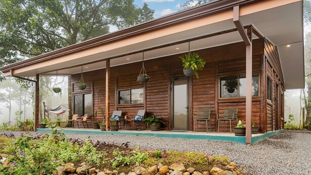 Eine rustikale Holzhütte mit überdachter Veranda, Sitzgelegenheiten im Freien und hängenden Pflanzen.