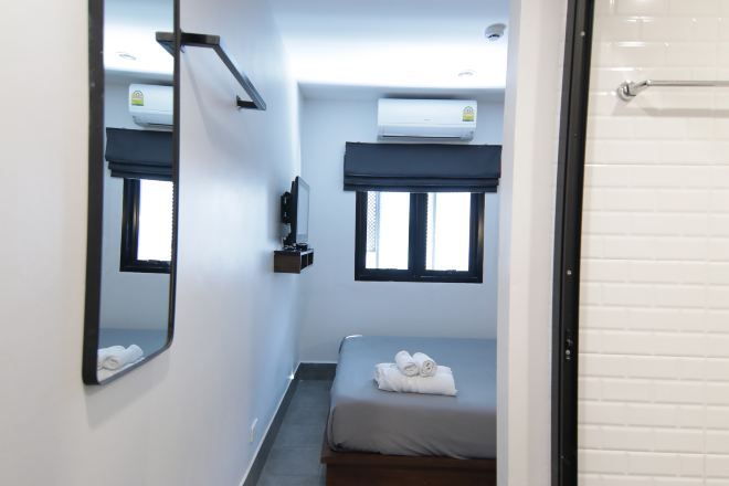 Una habitación pequeña y limpia con cama, espejo, ventana y aire acondicionado.