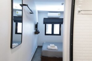 Una habitación pequeña y limpia con cama, espejo, ventana y aire acondicionado.