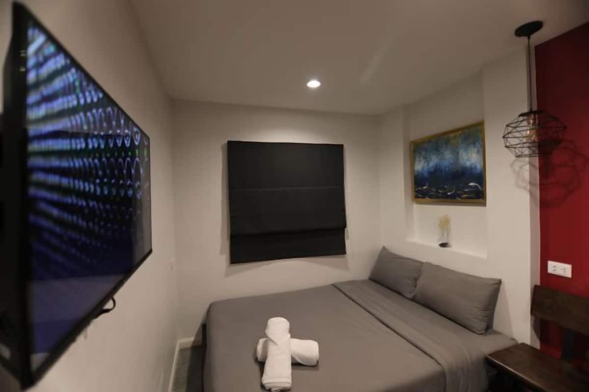 Een slaapkamer met een bed, een flatscreen televisie, een schilderij en een rode accentmuur.