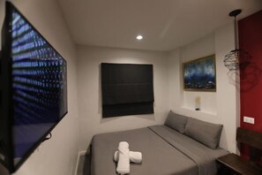 Ein Schlafzimmer mit einem Bett, einem Flachbildfernseher, einem Gemälde und einer roten Wand als Gestaltungselement.