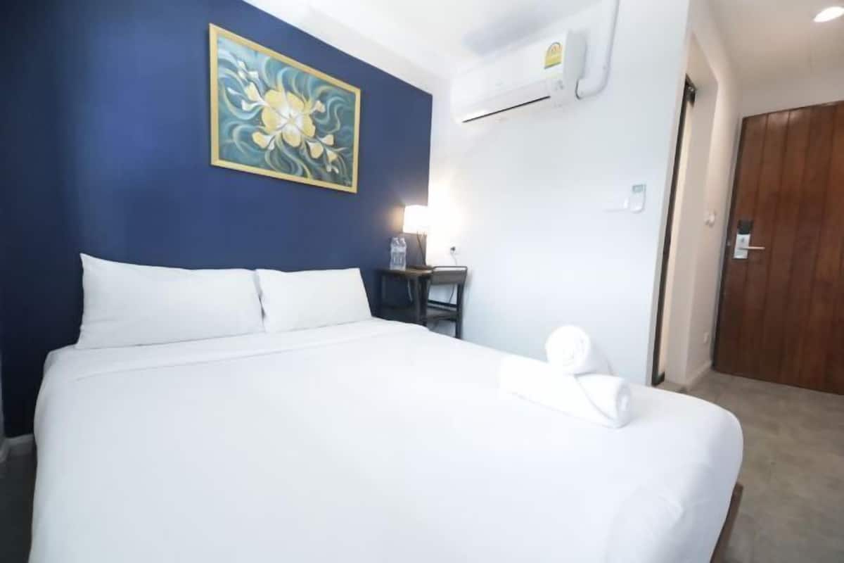 Een hotelkamer met een bed, nachtkastje, lamp, schilderij en een airconditioner.