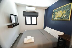 Ein Hotelzimmer mit Bett, Fernseher, Klimaanlage, Fenster mit Jalousie und einem Bild an der Wand.