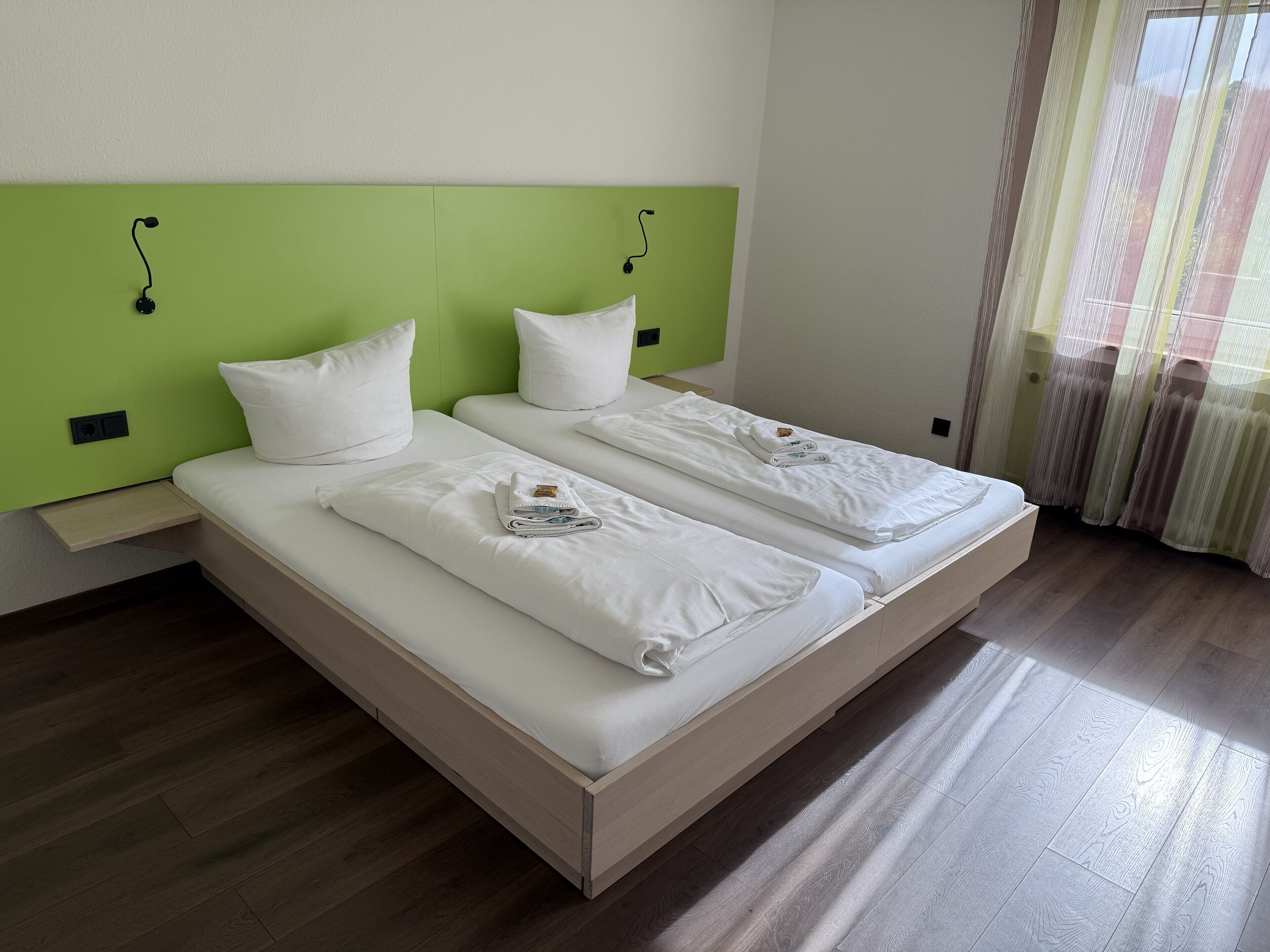 Una cama doble con sábanas y almohadas blancas, cabecera verde y una mesita de noche.