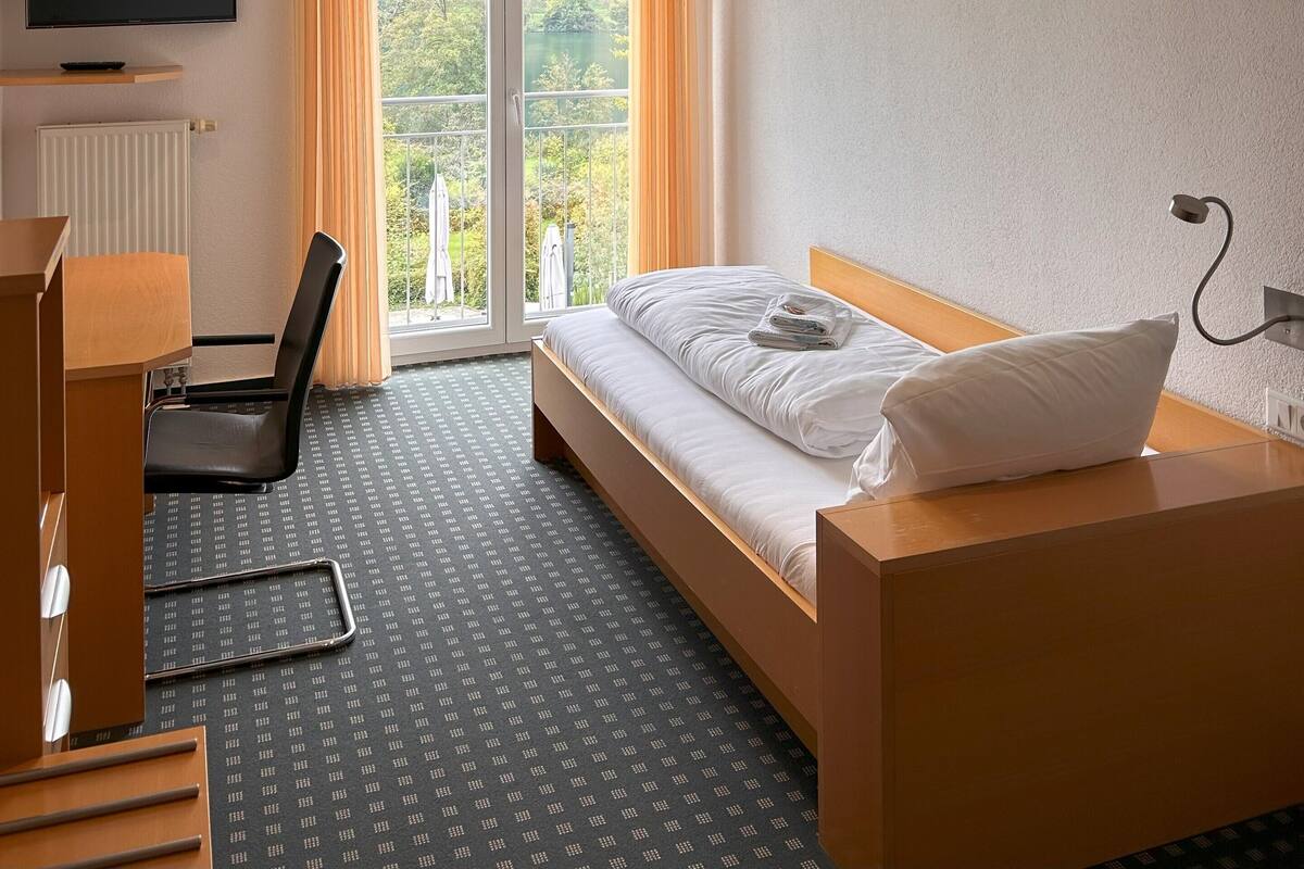 A hotel room with a bed, a desk, a chair, a TV, and a window with curtains.