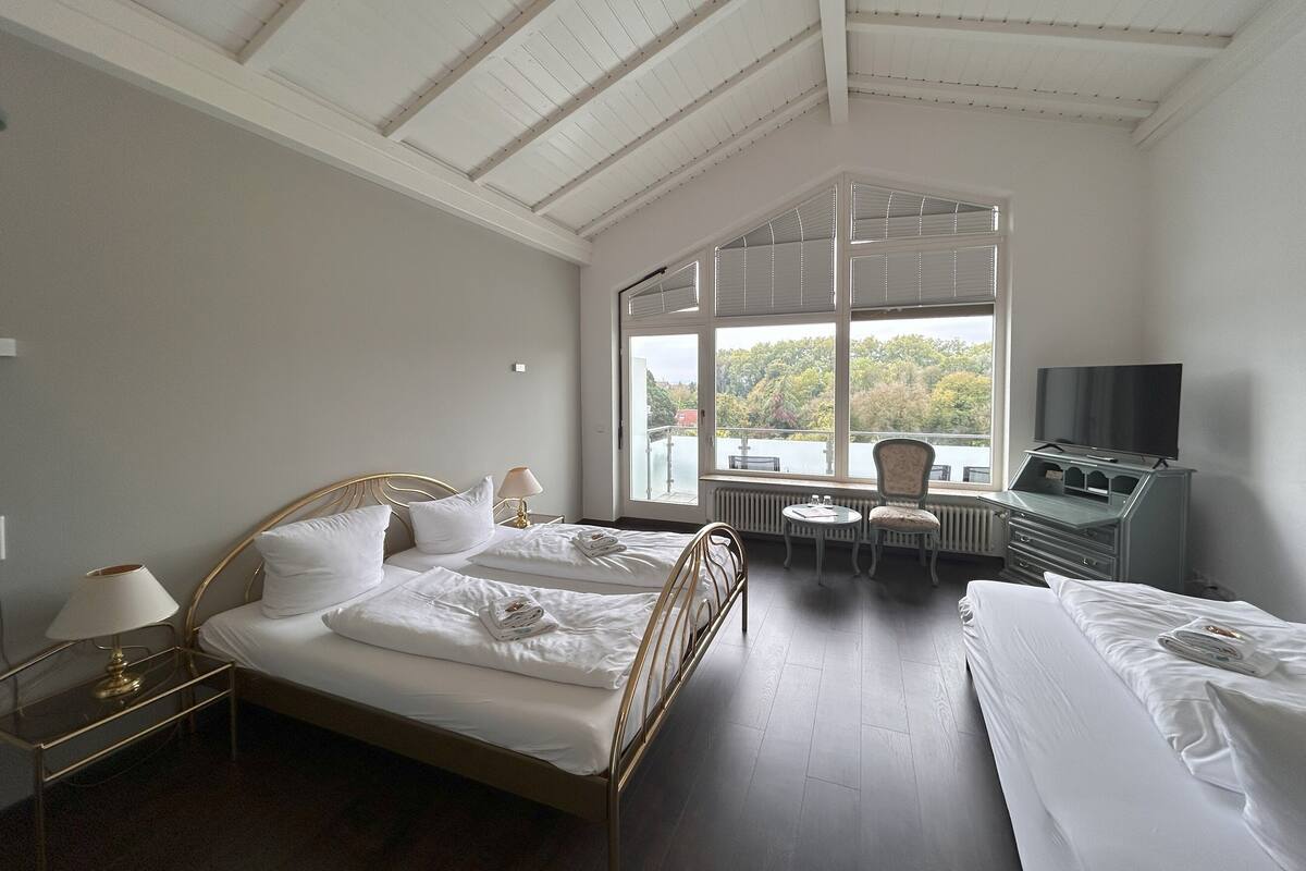 A hotel room with a large window, a bed, a desk with a TV, and a chair.
