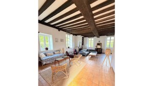 A spacious living room with a high ceiling, large windows, and a tiled floor.