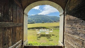 An arched doorway leading to an outdoor dining area with a table set for four, surrounded by a grassy landscape and hills in the background.