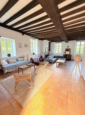 Uma sala de estar espaçosa com teto alto, janelas grandes e piso ladrilhado.