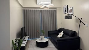 Ein modernes Wohnzimmer mit einer schwarzen Couch, einem runden Couchtisch, einem Flachbildfernseher und einer Zimmerpflanze.