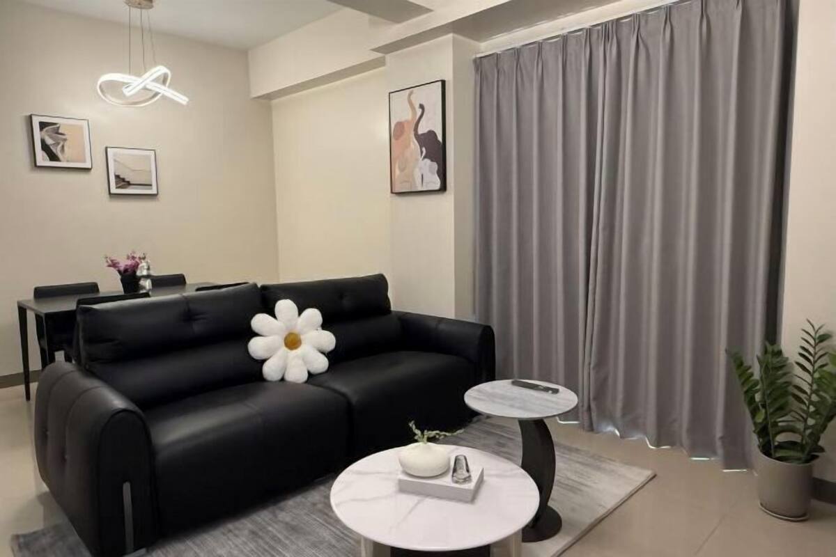 Ein modernes Wohnzimmer mit einer schwarzen Couch, einem runden Couchtisch und einem grauen Vorhang.