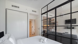 A modern hotel room with a large bed, a wardrobe, a glass partition, and a view of the kitchen and dining area. - Dubai Hills Sleeps 4 With Awesome Swimming Pool (Dubai)