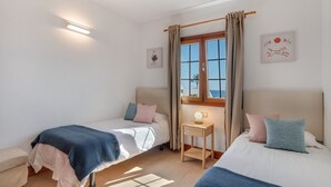 A bedroom with two beds, a bedside table with a lamp, a window with curtains, and wall art.