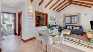 A modern living room with a glass dining table, blue sofa, and wooden beams on the ceiling.