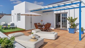 A patio with a white sofa, a dining table, and chairs, a covered area with a blue roof, and potted plants.